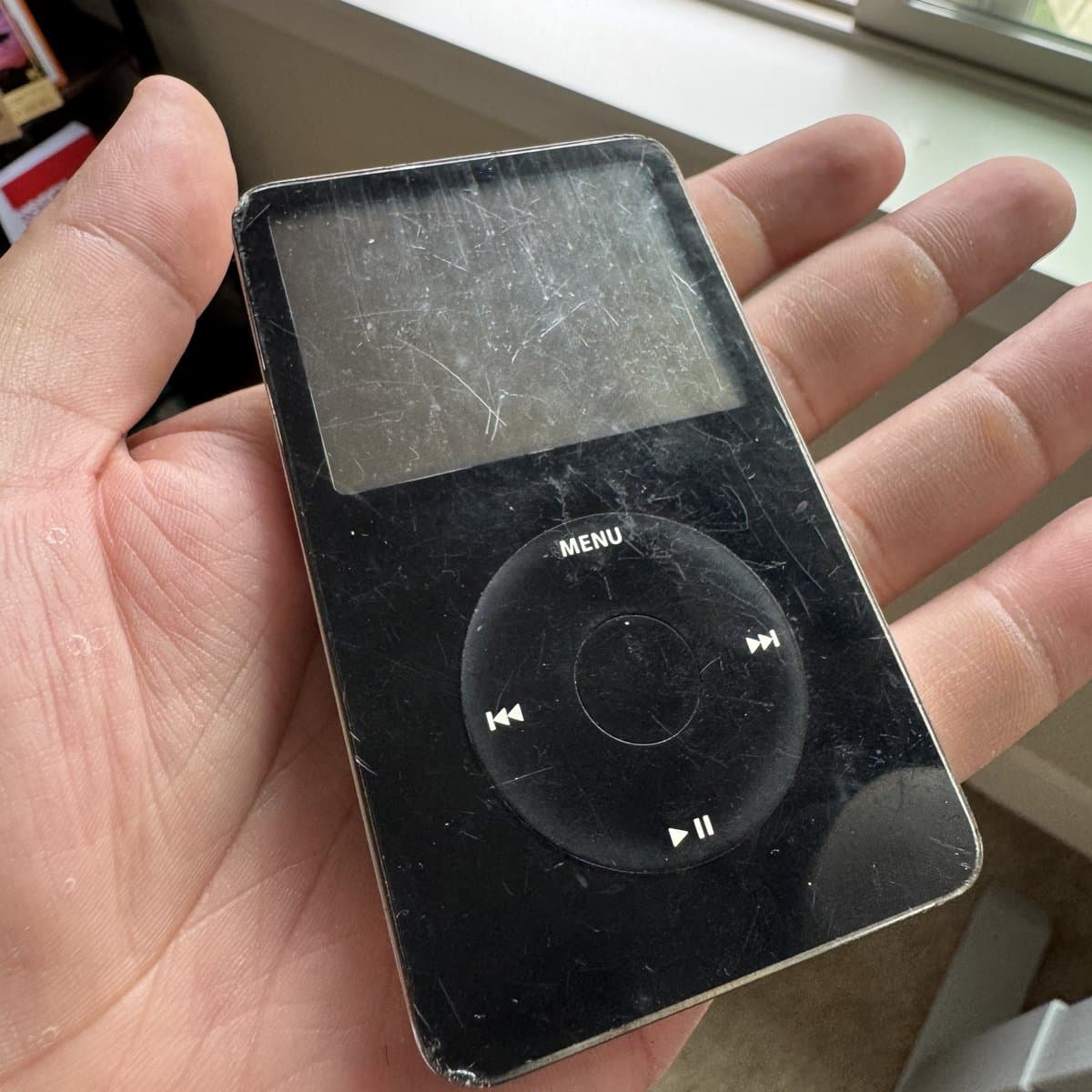 The real iPod in Russell's palm: black, heavily scratched, click wheel intact